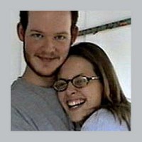 Young man with dark hair and facial hair hugging a laughing brunette young woman with glasses